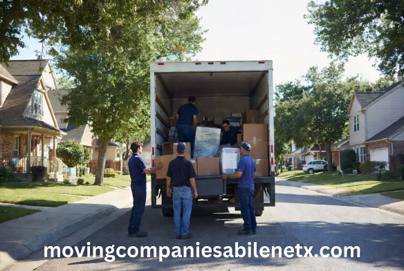 "Professional movers in blue uniforms organizing and loading cardboard boxes into a moving truck in a residential neighborhood."